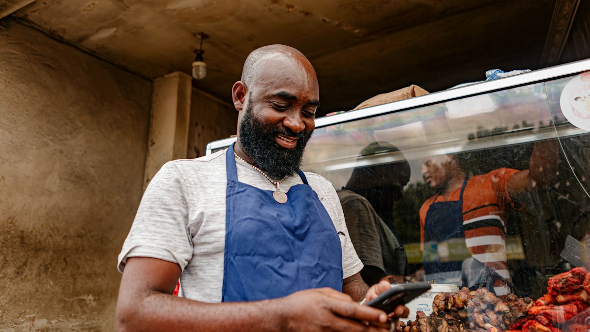 Vendedor de un puesto de comida sonríe mientras usa su teléfono para registrar una venta