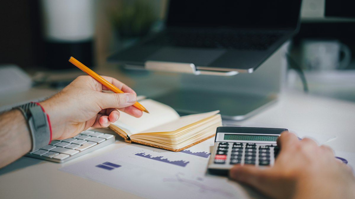 Persona calculando con una calculadora y una libreta el costo y la ganancia de un proyecto