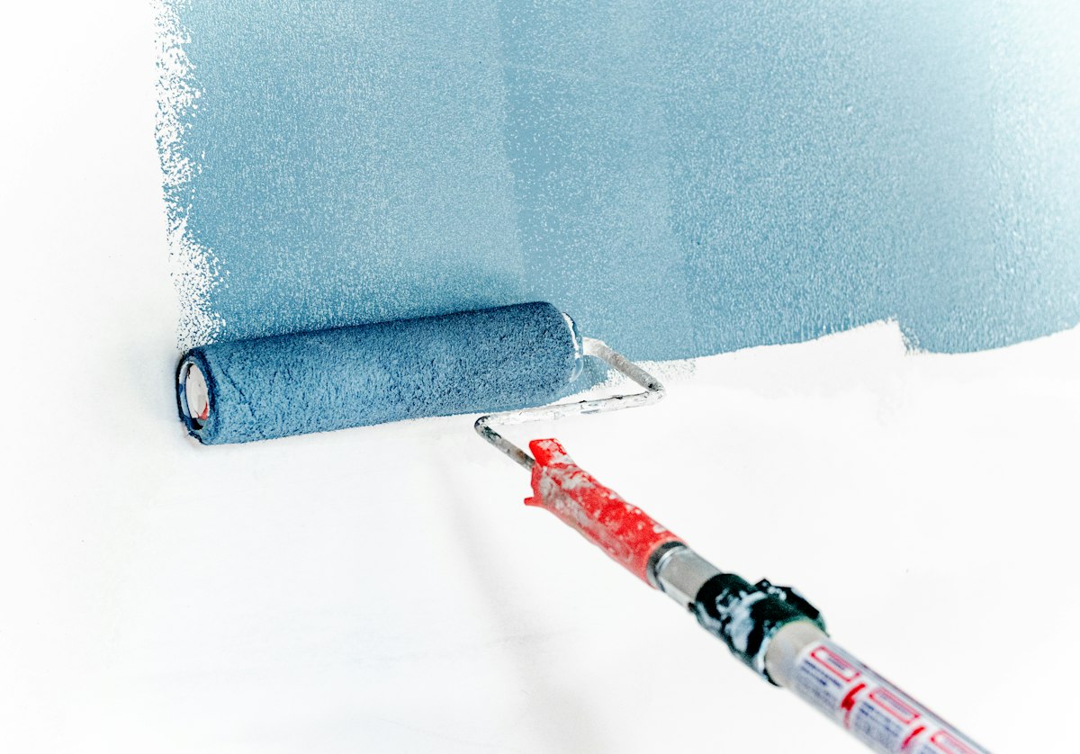Pintor aplicando pintura azul con un rodillo en una pared interior blanca