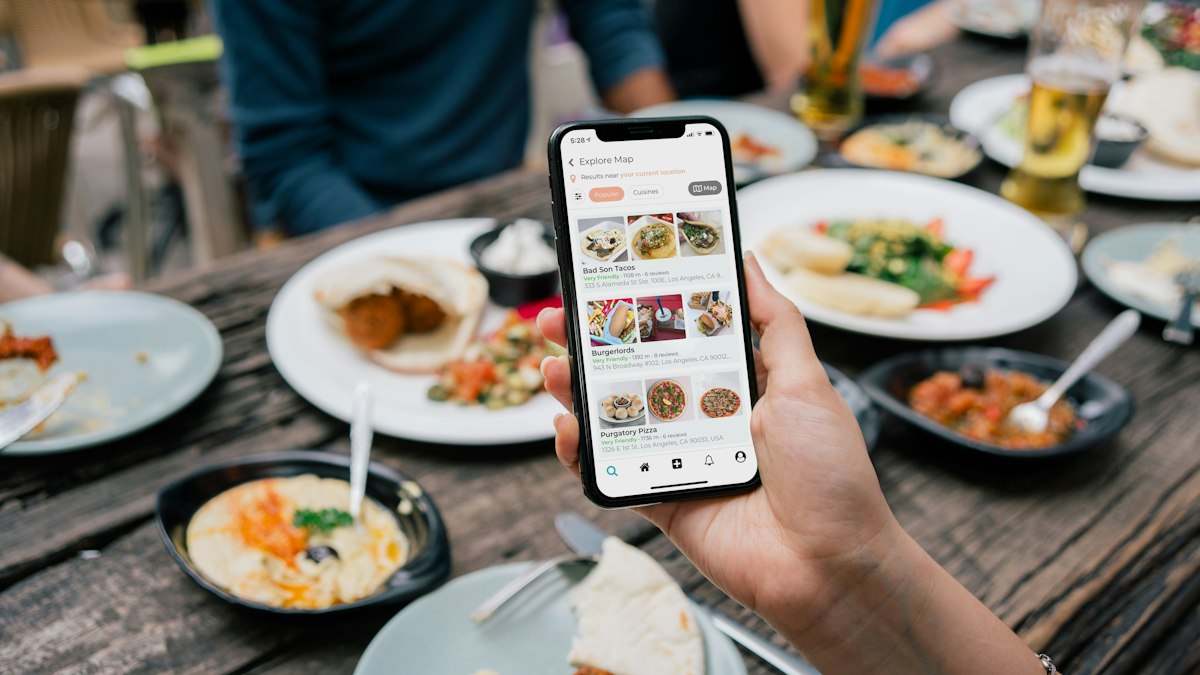 Persona sosteniendo un teléfono con un menú digital de restaurantes sobre una mesa con platos